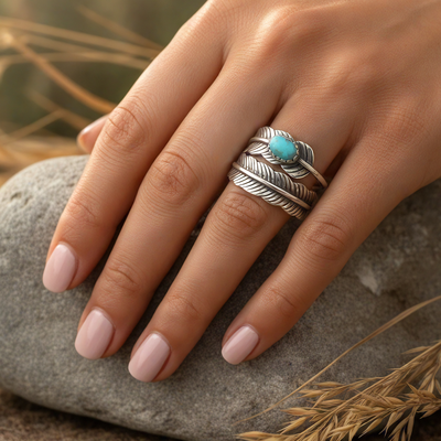 The feather ring worn on a hand resting on a smooth stone, its blue howlite catching the light