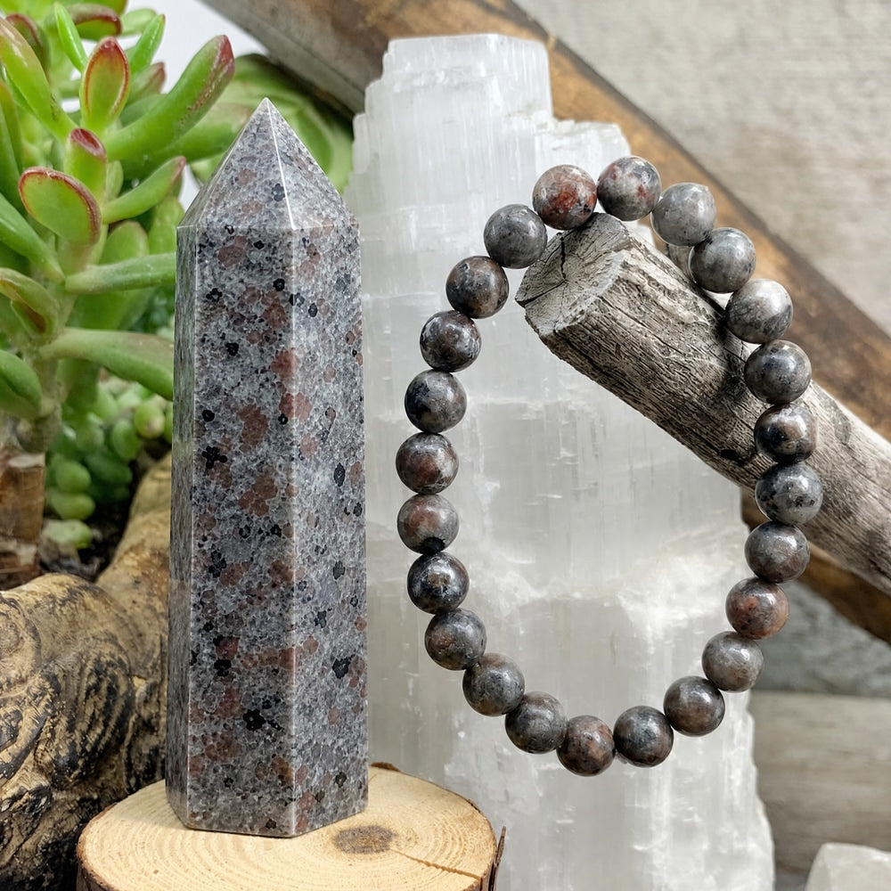 A grey Yooperlite point speckled with rust and black beside a Yooperlite bead bracelet hung on driftwood, in daylight