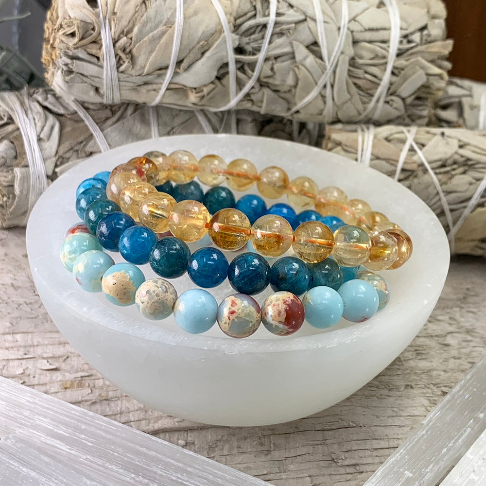 Brazilian citrine, apatite and azure variscite bead bracelets resting together in a white selenite bowl