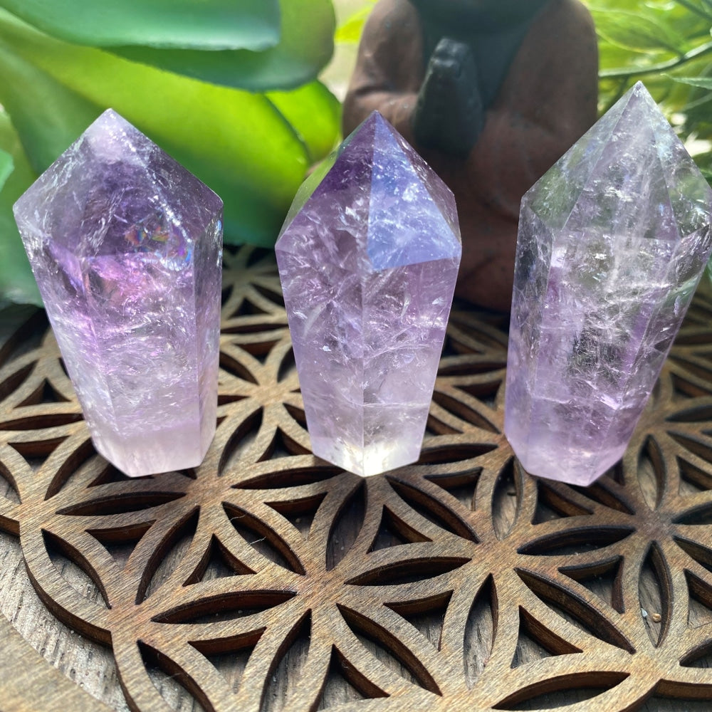 Three amethyst wands in different shades of lavender standing on a wooden flower-of-life board