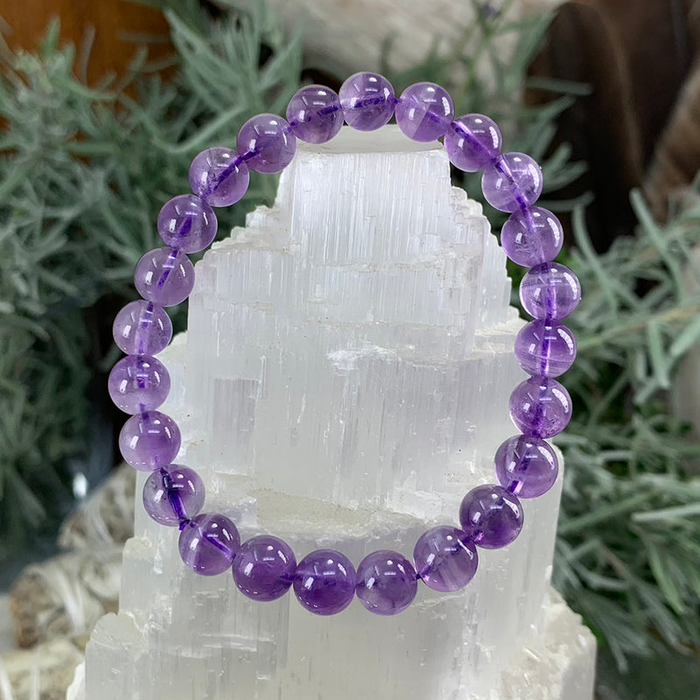 A round-bead amethyst bracelet draped over a white selenite tower