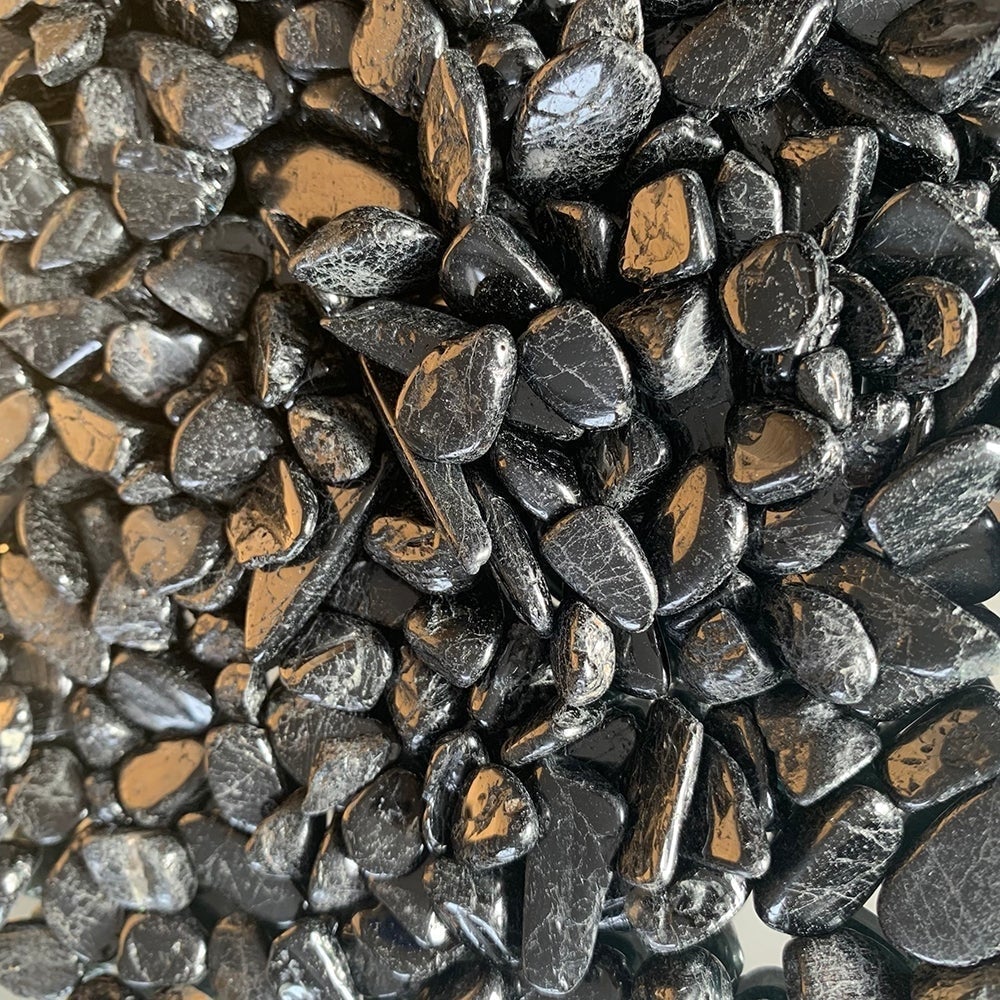 Close-up of many small tumbled black tourmaline stones with glossy, finely lined surfaces