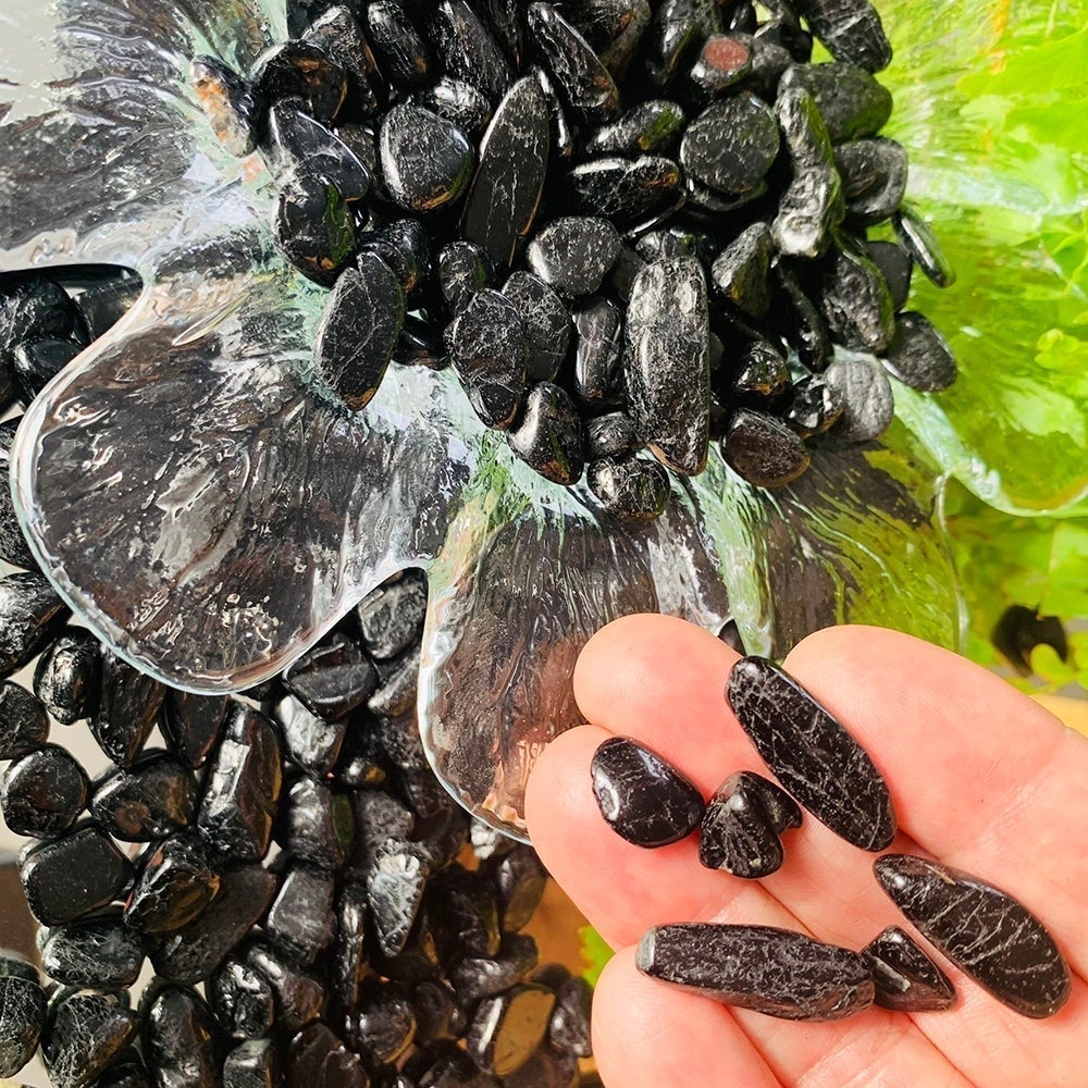 A few black tourmaline mini stones resting on fingertips beside a glass dish full of them
