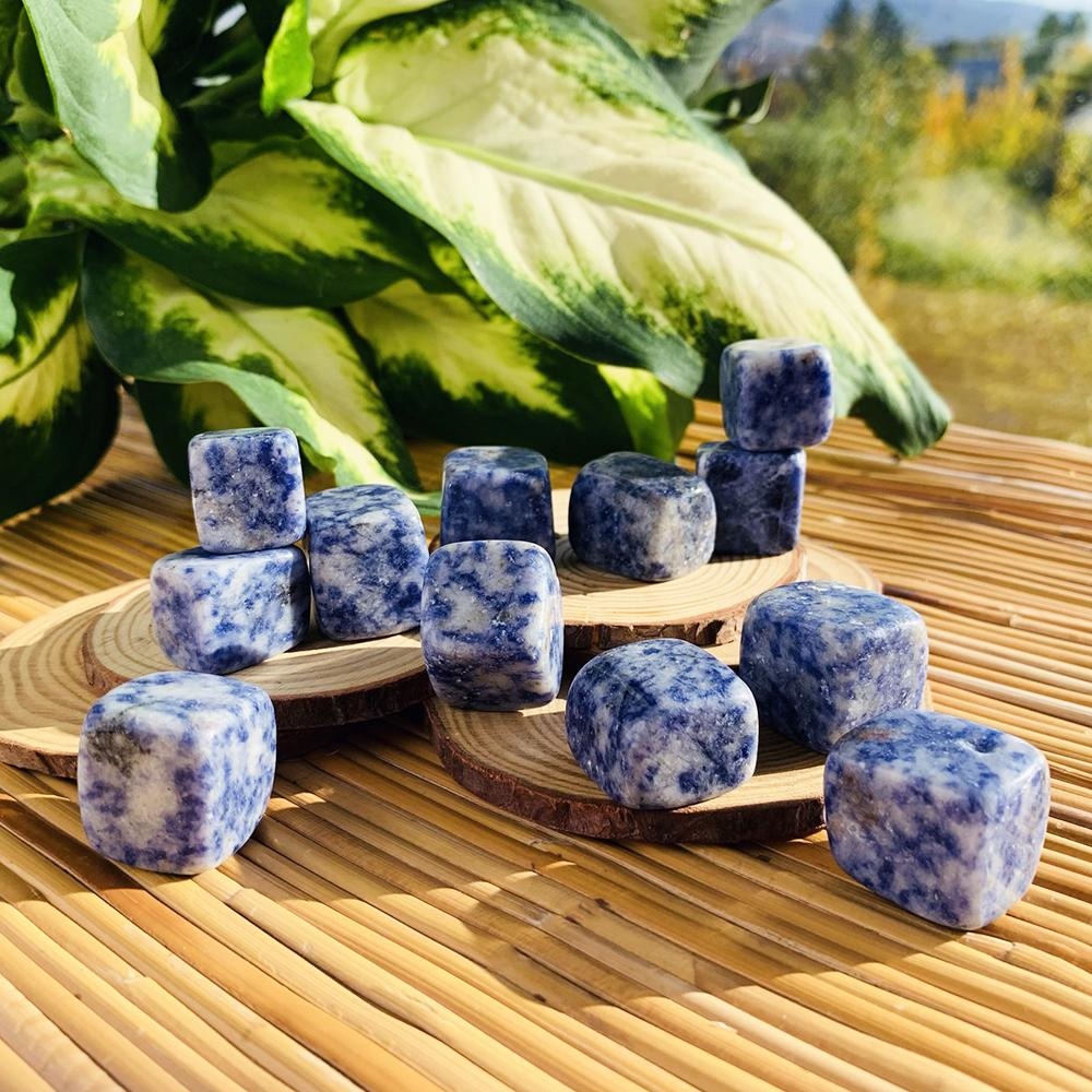 Blue spot jasper tumbled cubes, creamy white mottled with deep blue, stacked on wood slices in sunlight