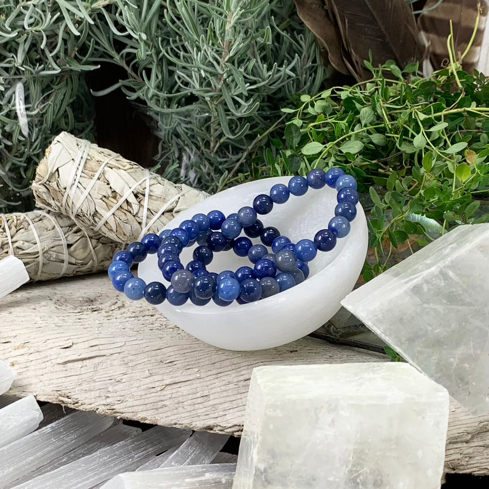 Blue aventurine mala bracelets of round beads in shades of deep and soft blue, resting in a white selenite bowl