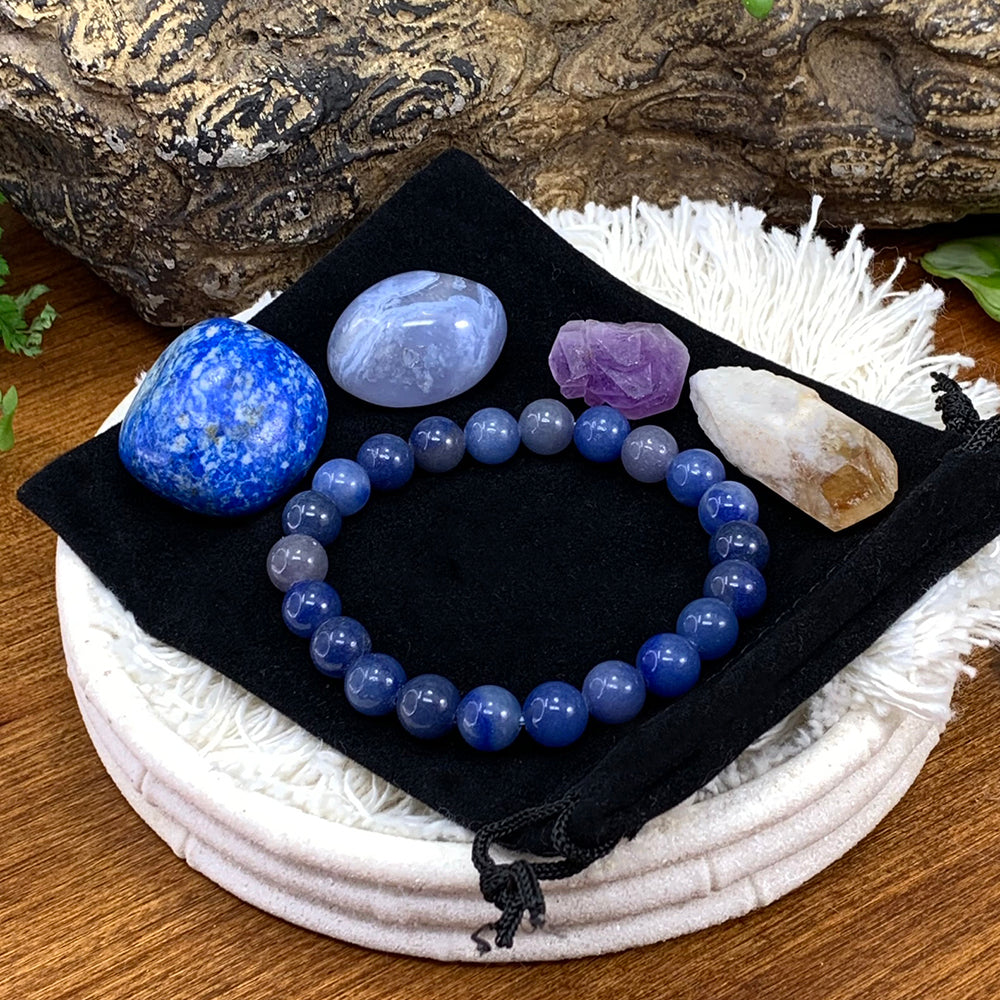 The blue aventurine mala bracelet laid on a black velvet pouch with a lapis lazuli tumbled stone, a blue lace agate tumbled stone, an amethyst fairy cluster and a citrine shard