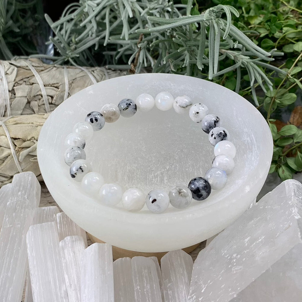Moonstone mala bracelet of milky white and grey-black flecked beads resting in a selenite bowl