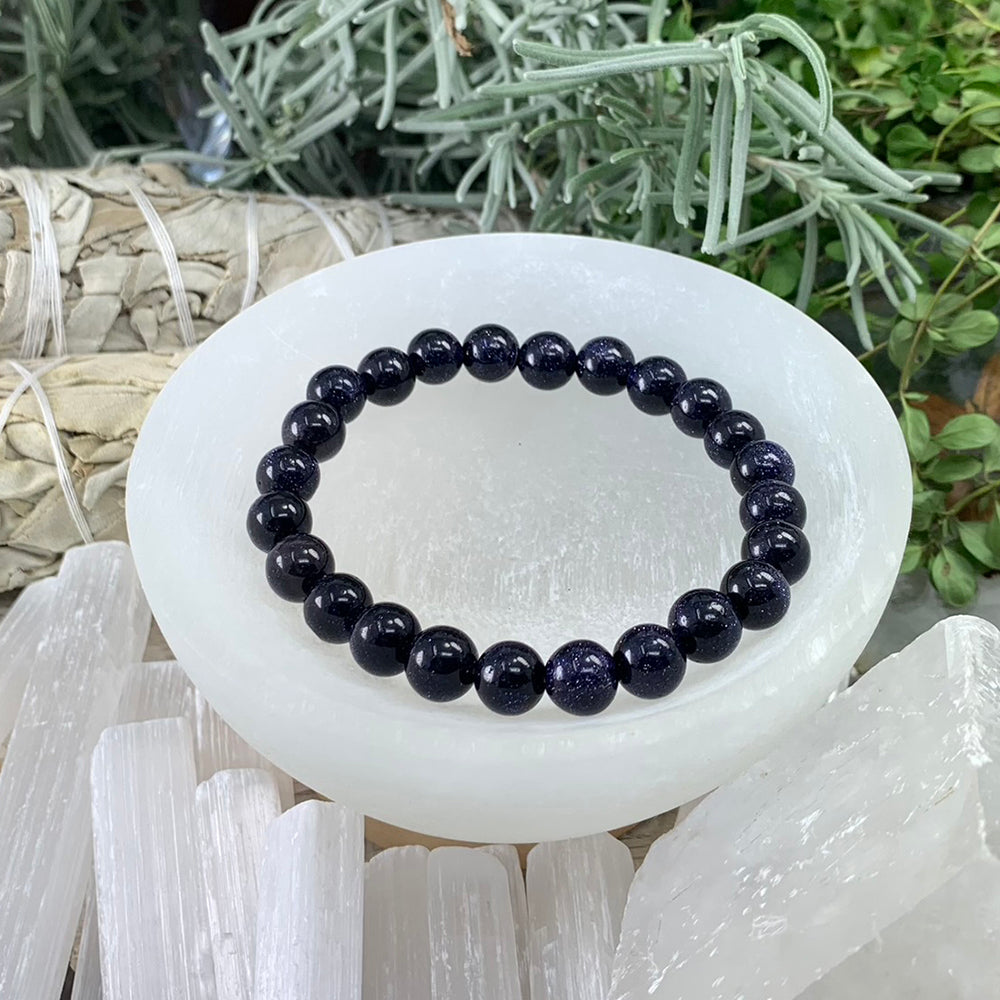 A blue sandstone bead bracelet, deep navy beads with glittering flecks, resting in a selenite bowl