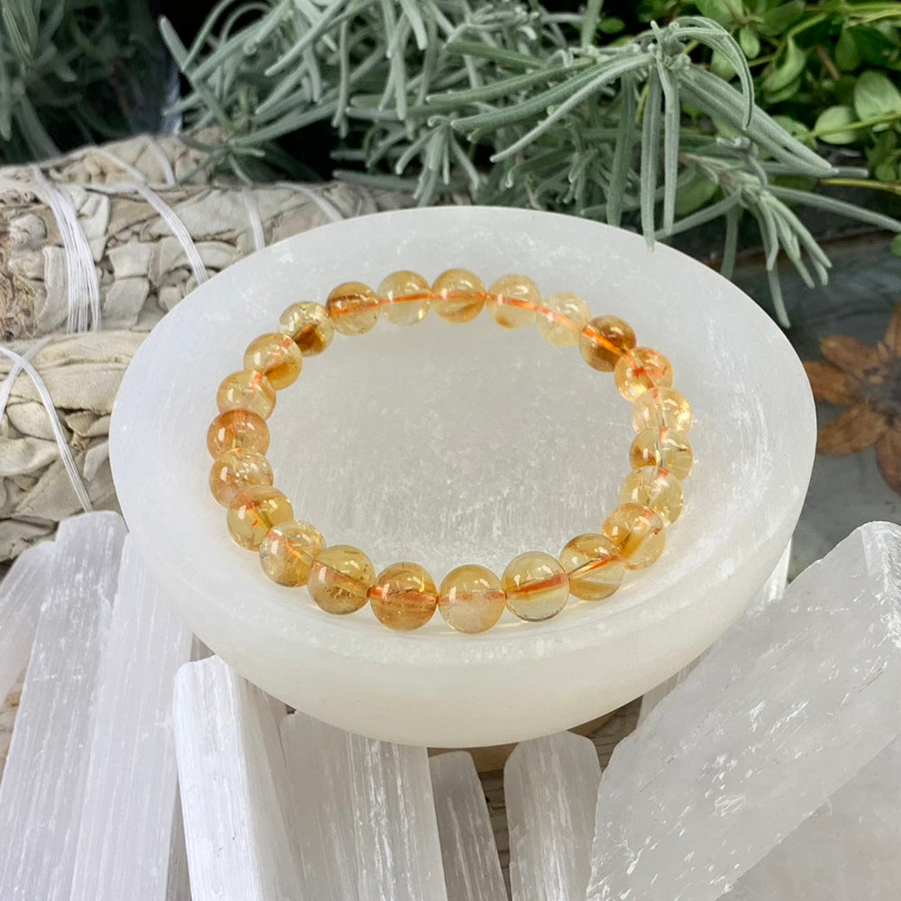 A Brazilian citrine mala bracelet of round, clear golden beads resting in a white selenite bowl