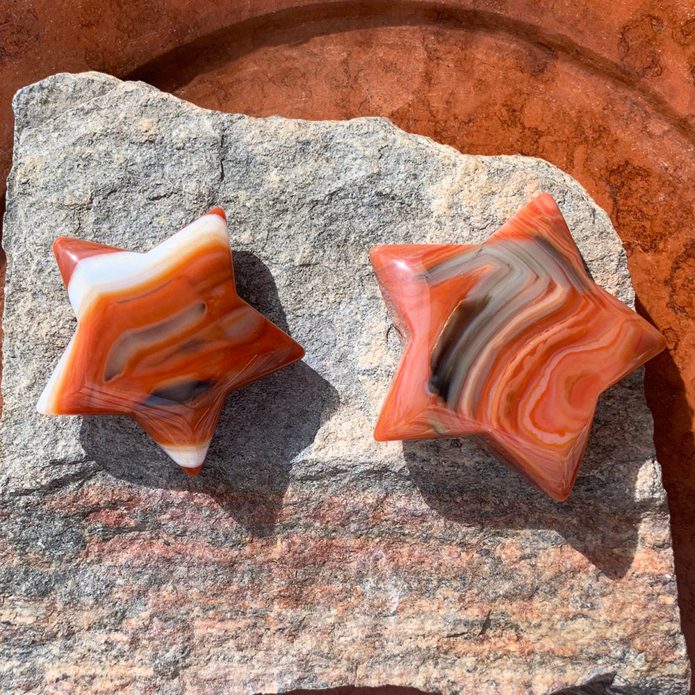 Two carnelian stars on a speckled stone slab, each with its own swirl of orange, red, cream and gray