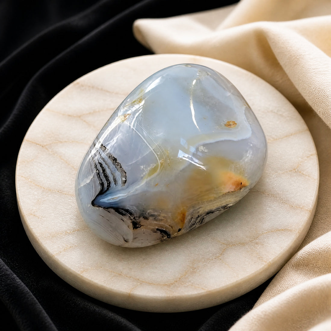 A polished oval chalcedony palmstone, cloudy blue-gray with dark swirls, on a pale marble dish