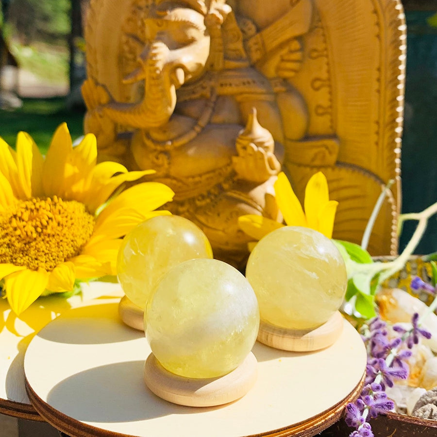 Three translucent citrine spheres glowing on wooden stands in front of a carved statue and sunflowers