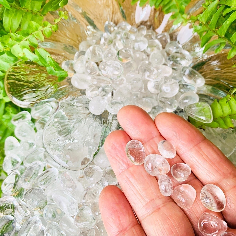 A few clear quartz mini gemstones resting on fingertips above a glass bowl filled with more