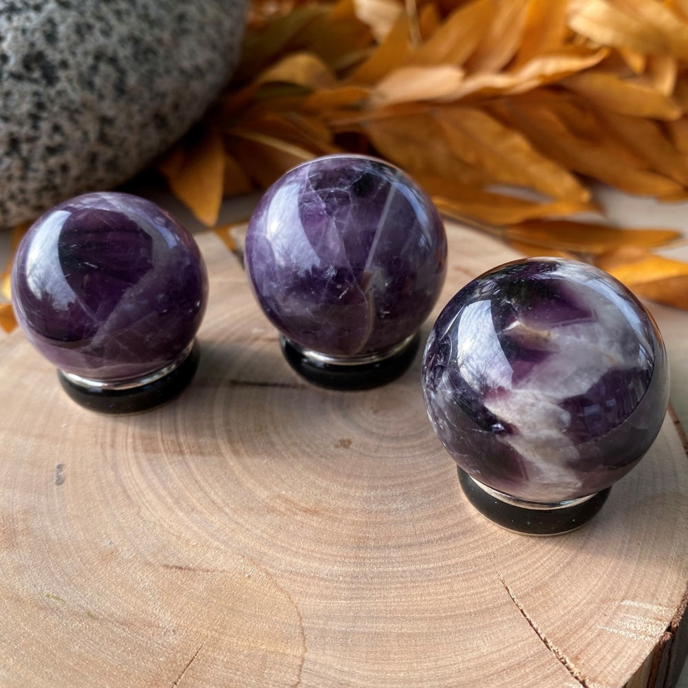 Three polished dream amethyst small spheres with deep purple and white chevron banding on a wooden slice