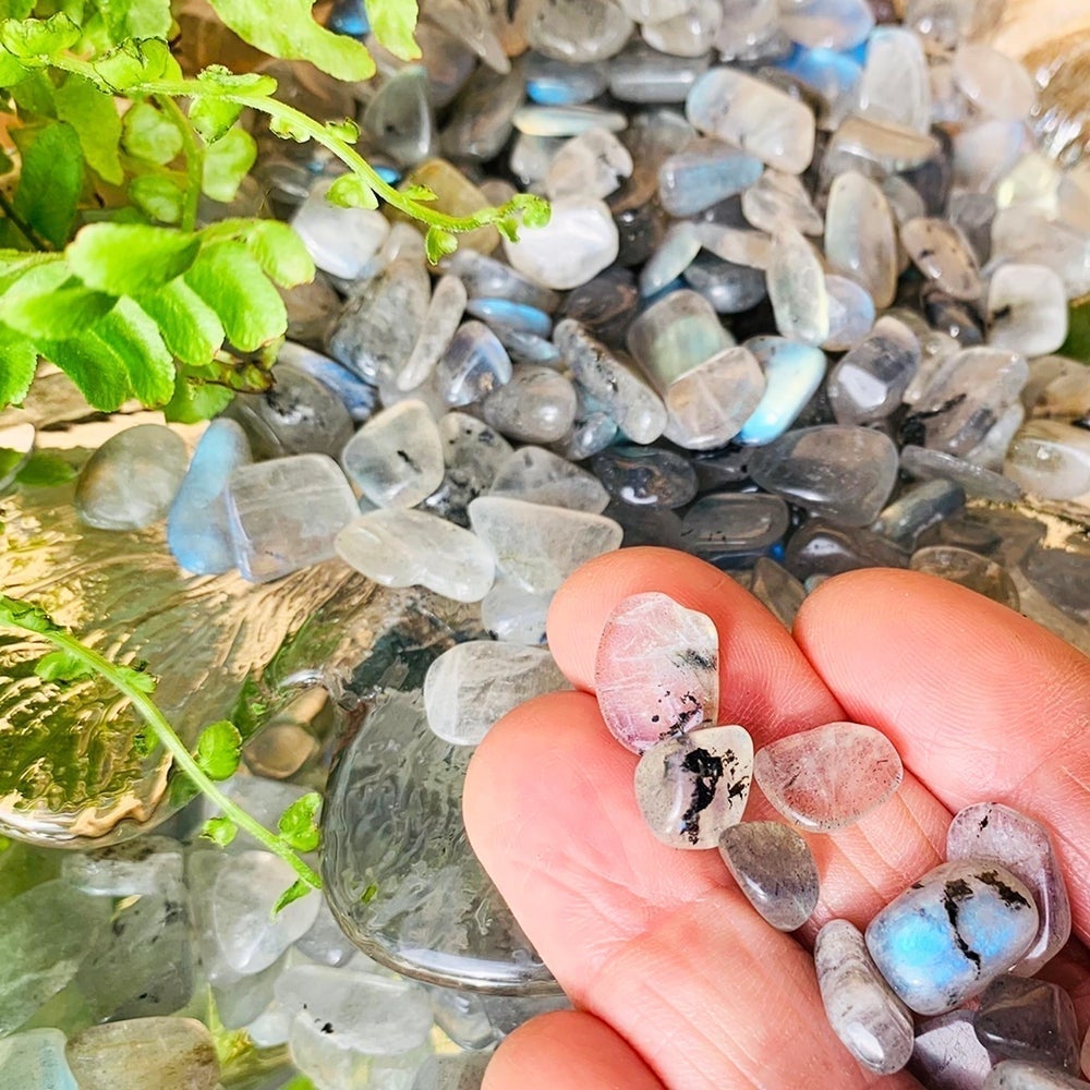 A few flash labradorite mini gemstones on fingertips above a pile of more, one glowing blue
