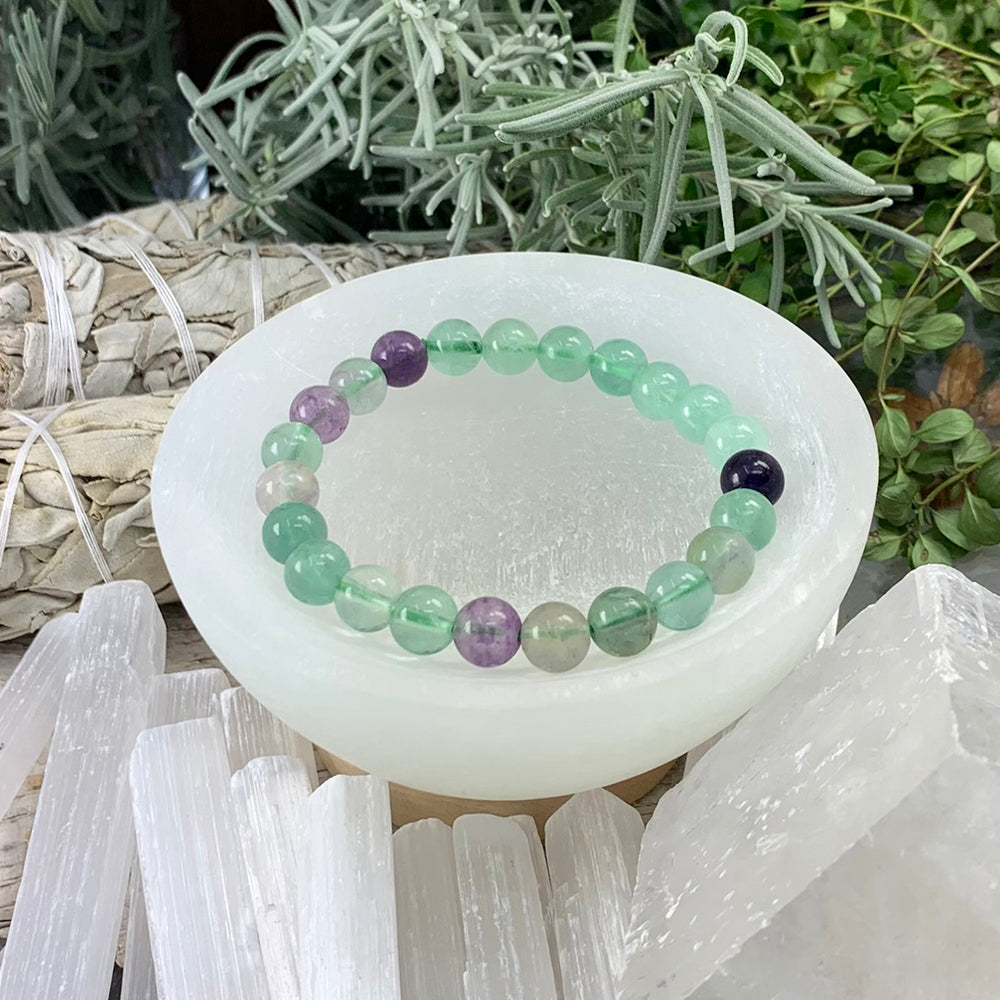 Fluorite mala bracelet of translucent sea-green, clear and violet beads resting in a selenite bowl
