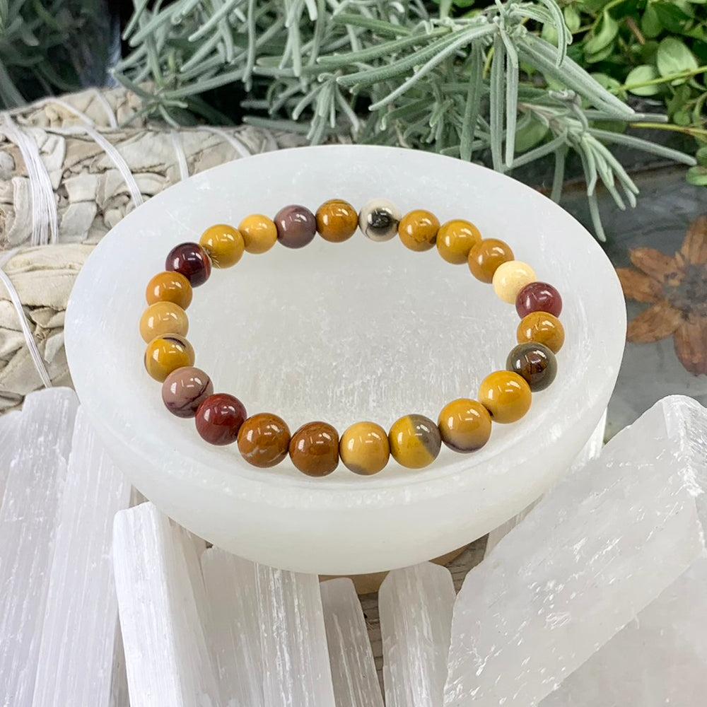 Golden mookaite jasper mala bracelet of mustard, ochre, cream and deep red beads resting in a selenite bowl
