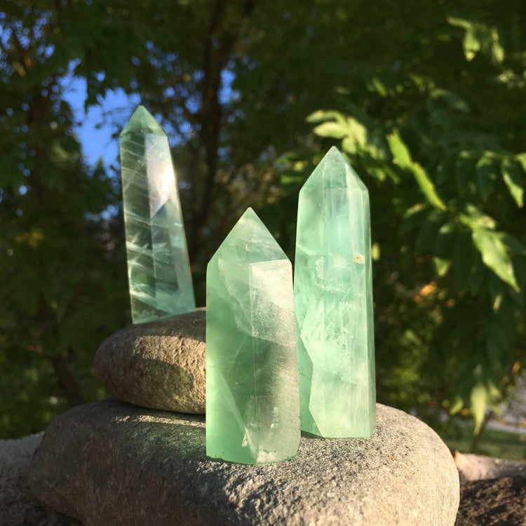 Three green fluorite points of different heights and shades standing on stacked stones in evening light