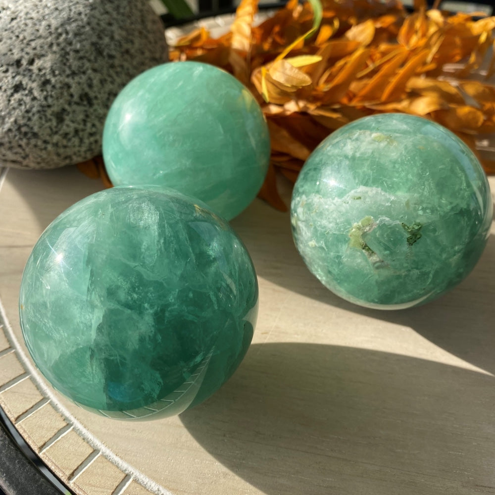 Three polished green fluorite spheres in sunlight, each with different green banding and inclusions