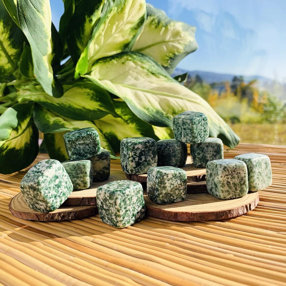 Green spot jasper tumbled cubes, white speckled with forest green, stacked on wood slices in sunlight