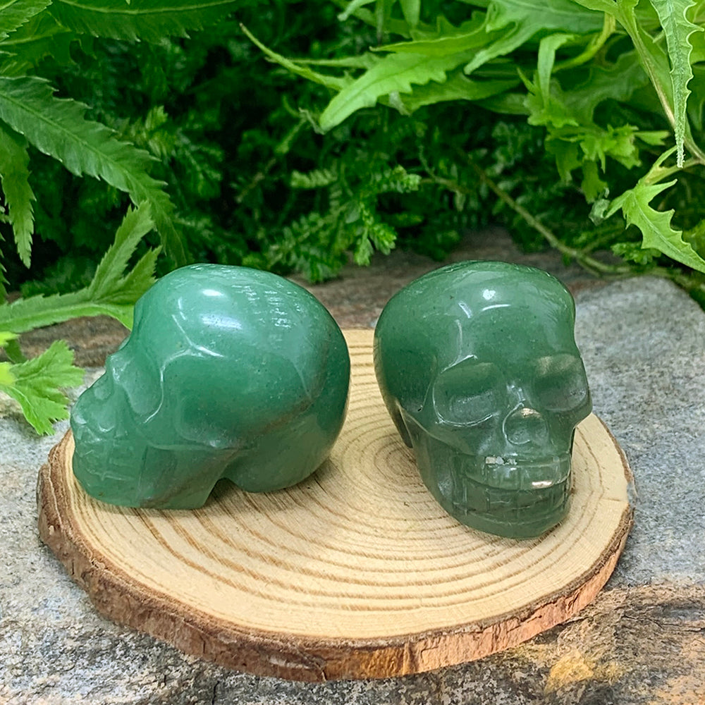 Two green quartz skull totems on a wooden slice, one in profile and one facing forward