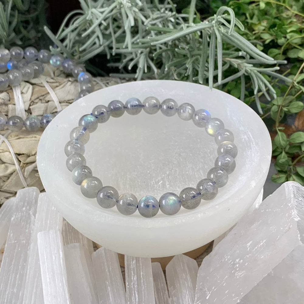 A grey moonstone bead bracelet resting in a selenite bowl, several beads flashing blue