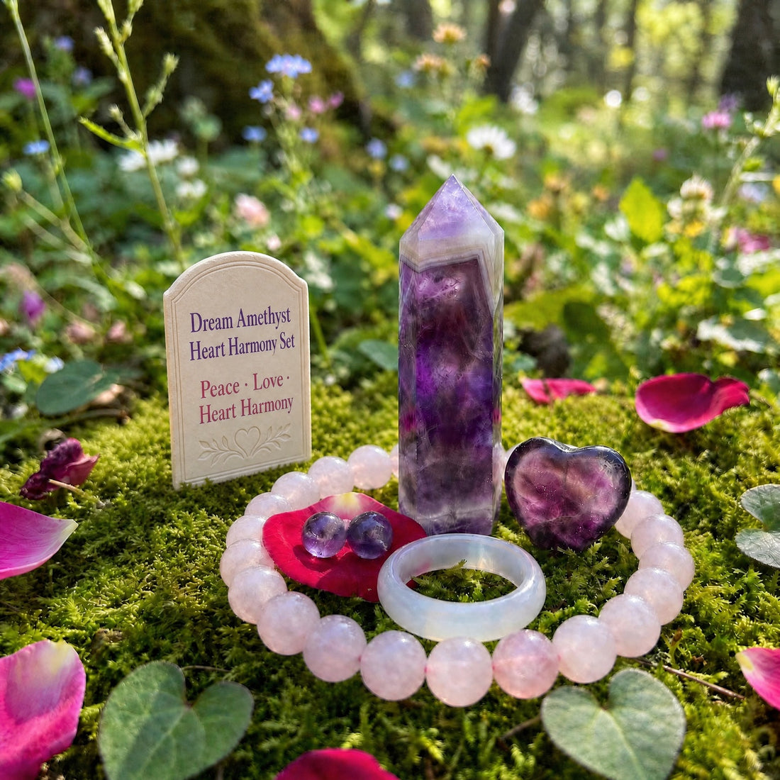 The five pieces together on moss: a dream amethyst point, a purple fluorite heart, a rose quartz bead bracelet, a pale pink agate ring and a pair of amethyst studs on a rose petal
