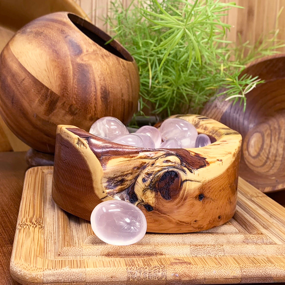 Polished pale pink ice rose quartz ellipse stones in a wooden bowl, with one resting in front