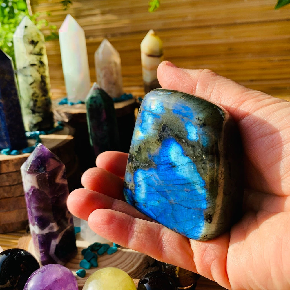 A polished labradorite freeform resting in an open palm, flashing electric blue in the sunlight