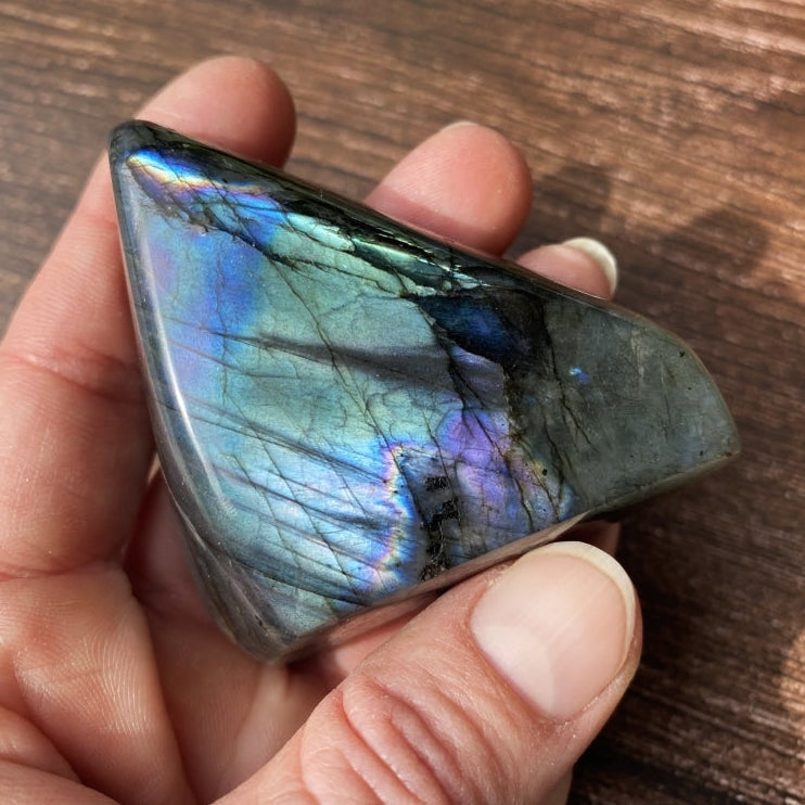 A triangular labradorite freeform held in the hand, flashing teal, violet and gold