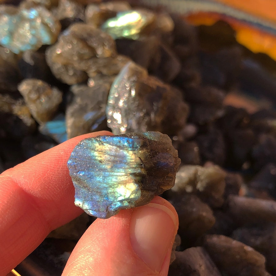 A small rough labradorite stone held between finger and thumb, flashing electric blue and gold