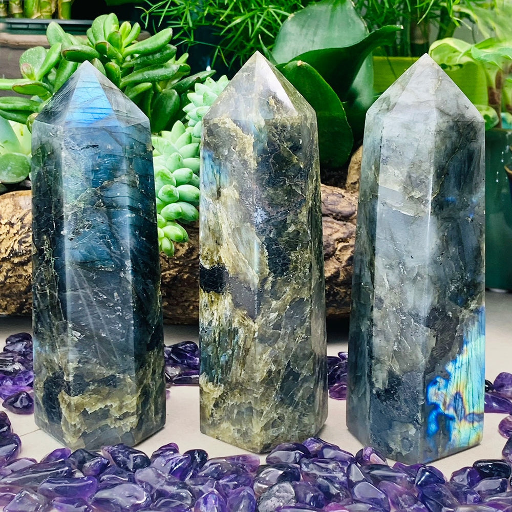 Three labradorite tall generators side by side on a bed of tumbled amethyst, each with a different pattern and flash