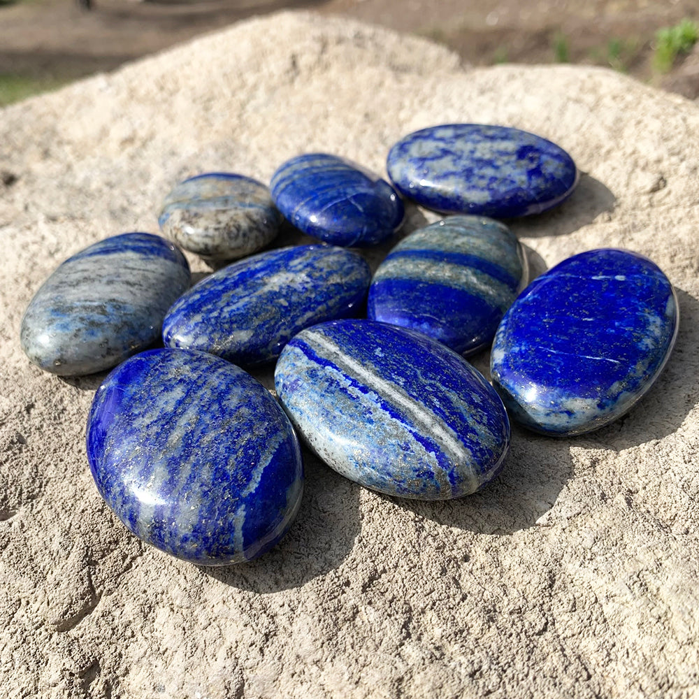 A group of lapis lazuli palmstones on sand, each with its own blue tone and white veining