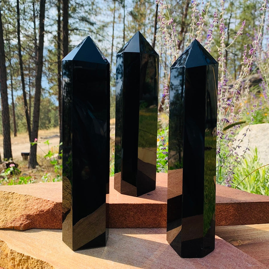 Three polished black obsidian generator towers standing on red sandstone outdoors, reflecting the trees and sky