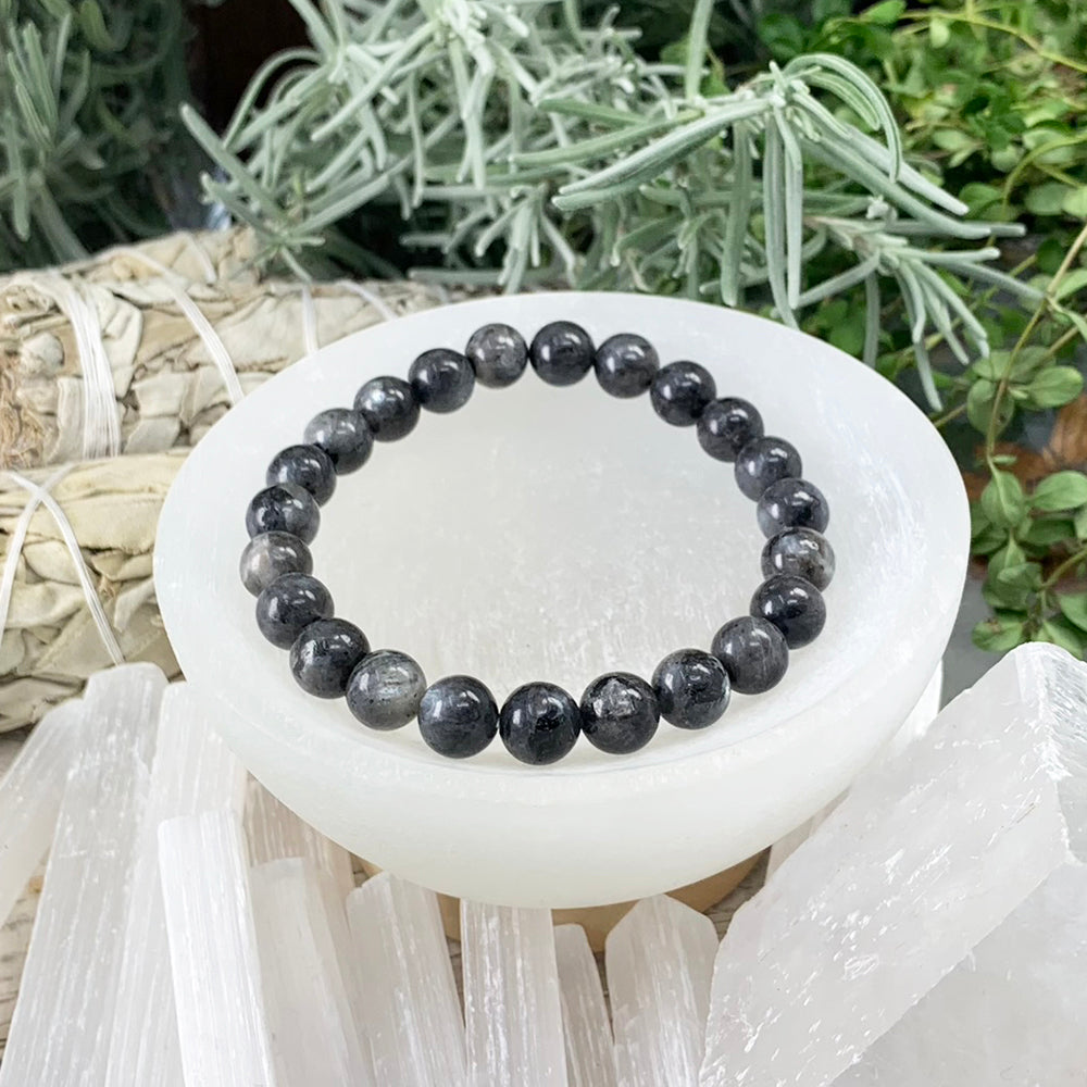 One larvikite mala bracelet of round dark grey beads with a silvery sheen, resting in a white selenite bowl