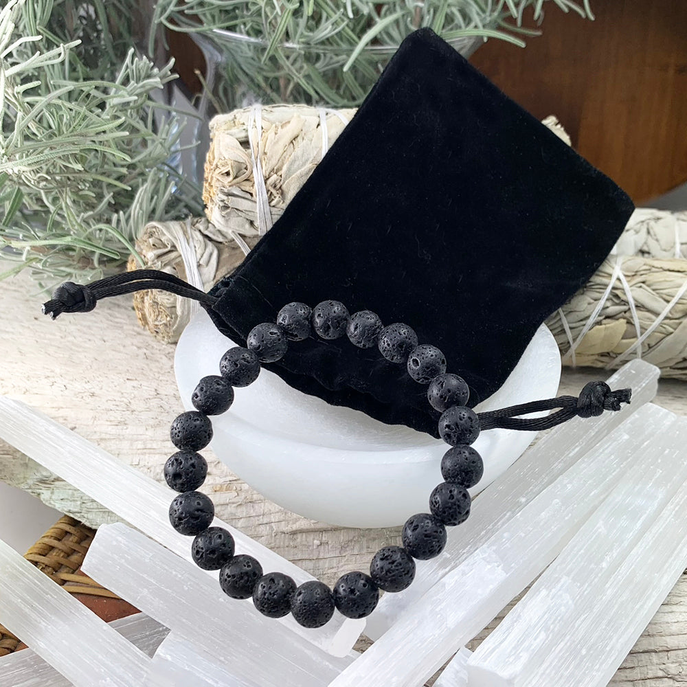 Lava stone bead bracelet resting in front of a black velvet drawstring pouch, with selenite sticks and sage
