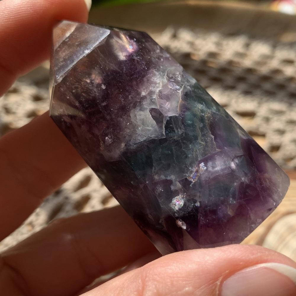 A short multicolor fluorite generator with violet, green and clear zones held between finger and thumb