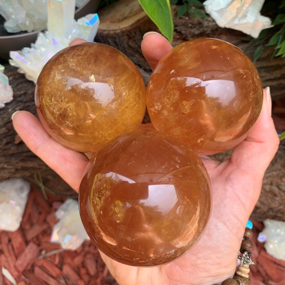 Three glossy orange calcite spheres held together in an open hand, glowing honey-orange with bright inner flecks