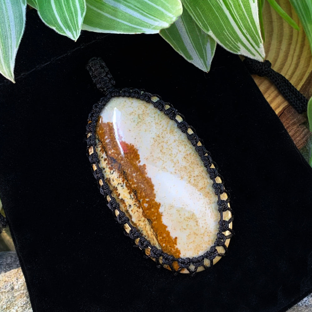 The picture jasper pendant resting on its black velvet pouch, showing the macramé knotwork around the stone