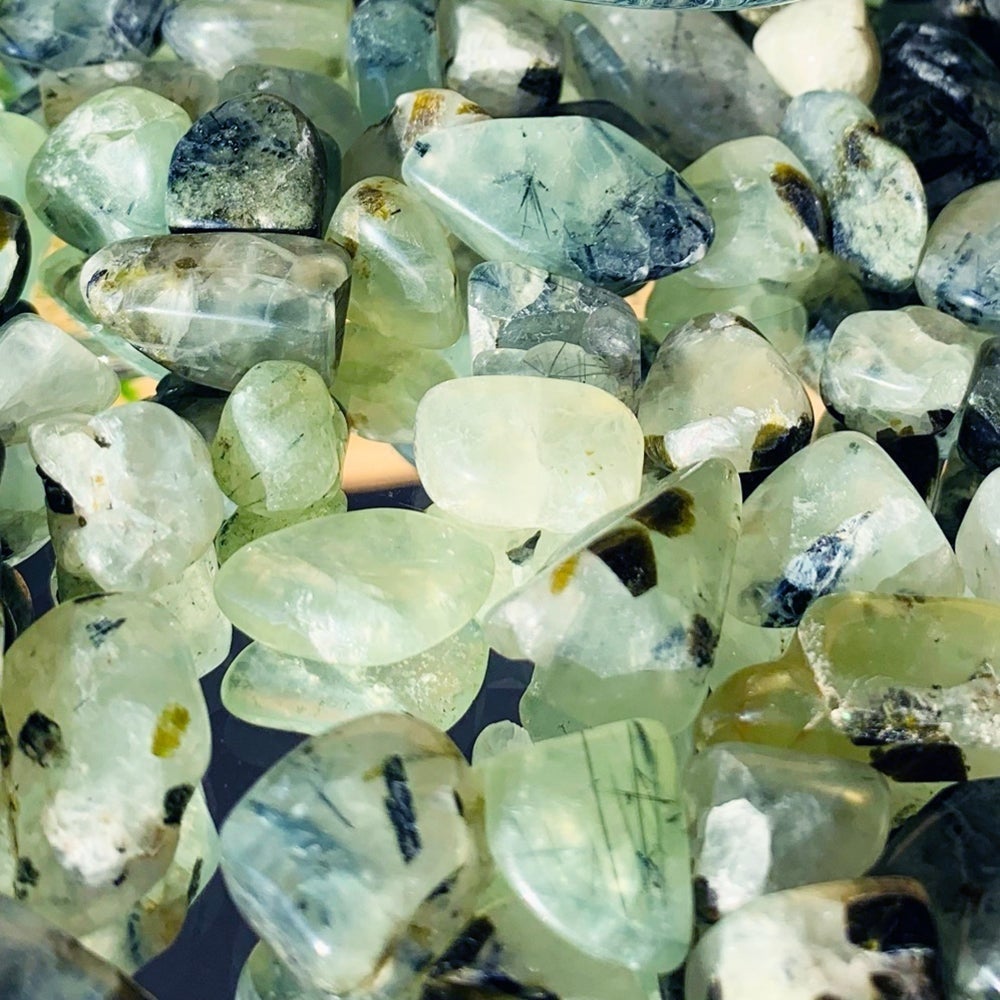 Close-up of translucent green prehnite stones with fine black tourmaline needles and flecks inside