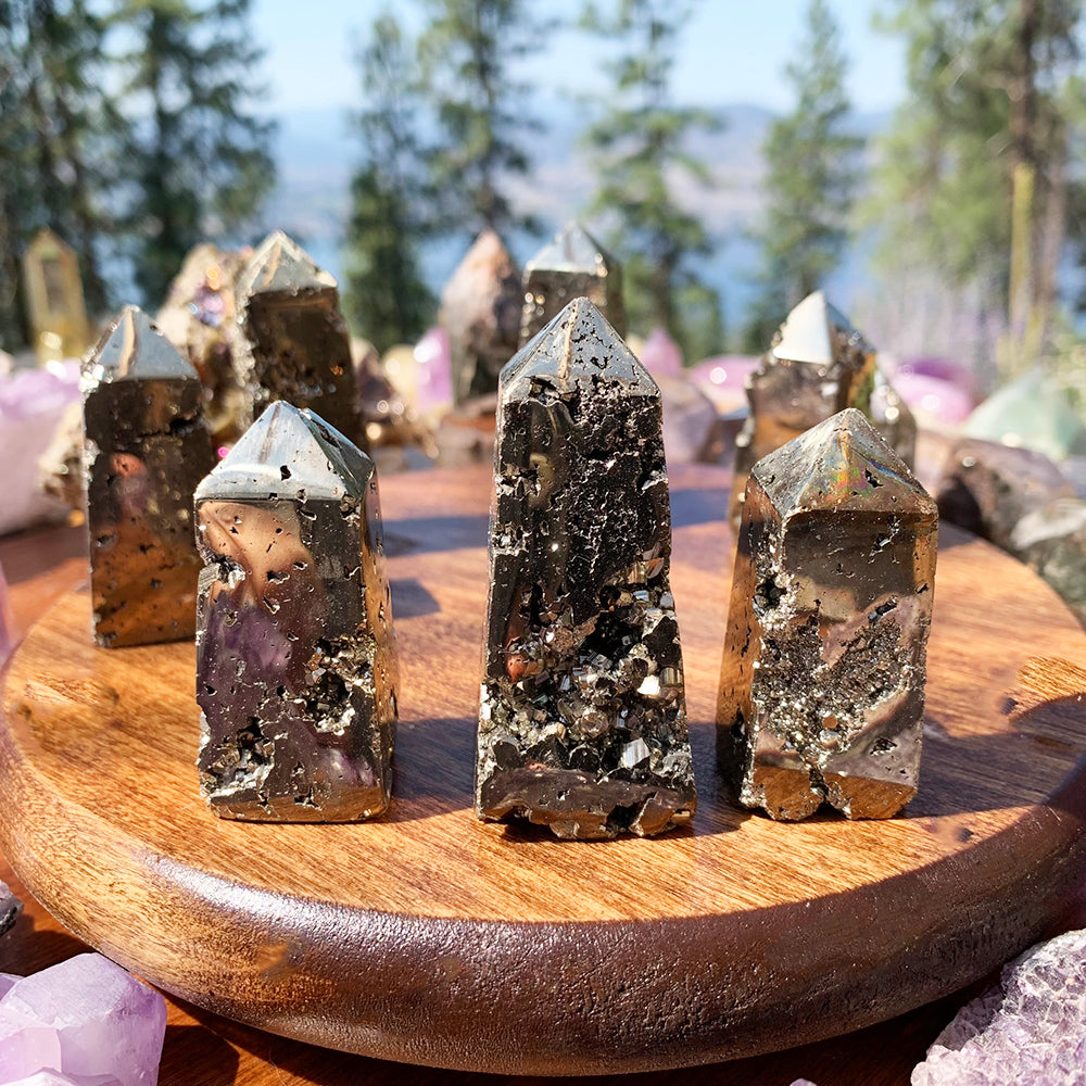 Several polished pyrite generators on a round wooden tray, their mirror-bright faces broken by raw, sparkling pyrite texture
