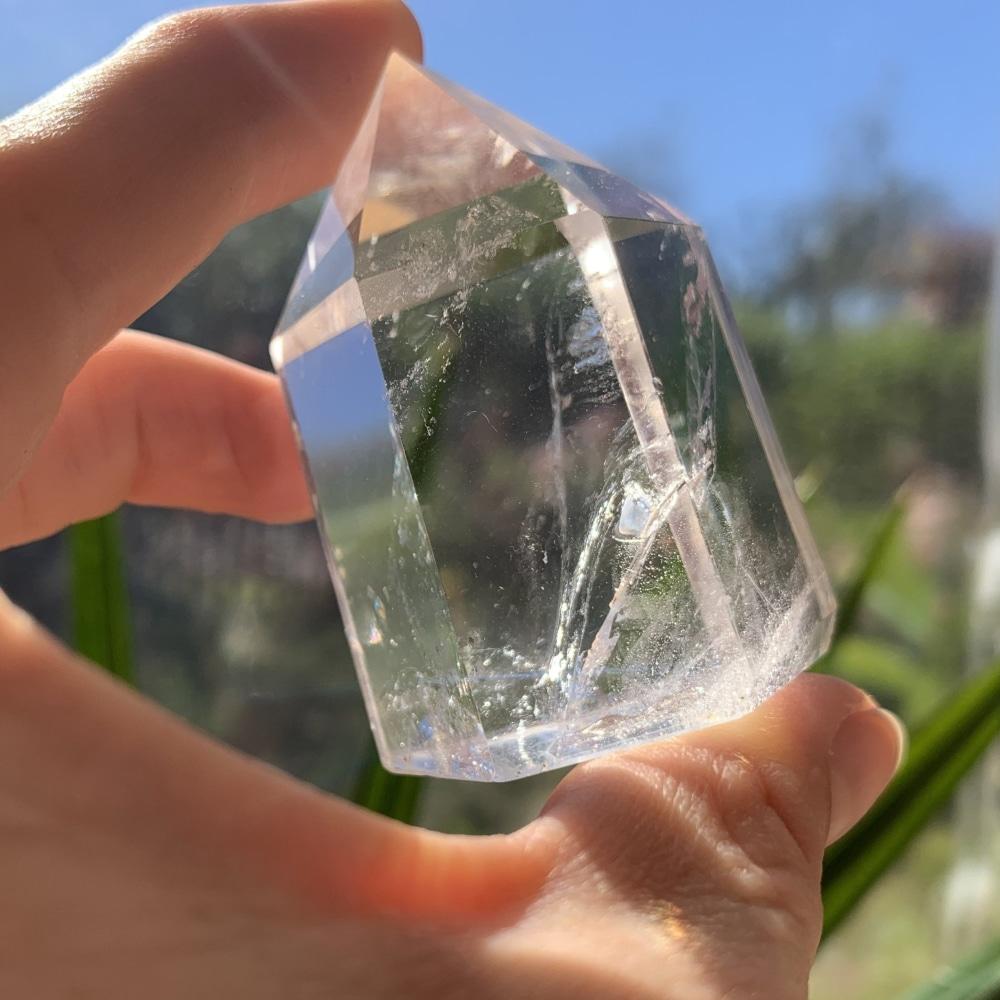 Short, thick clear quartz generator held between fingers in sunlight, showing its six-sided point and inner veils