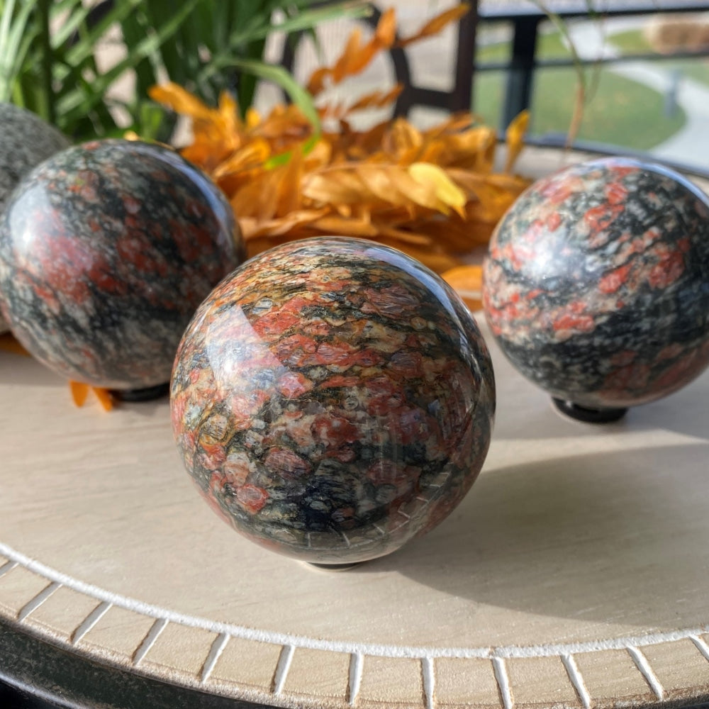Three polished red granite spheres on a tray, each with its own pattern of red, black and grey grains