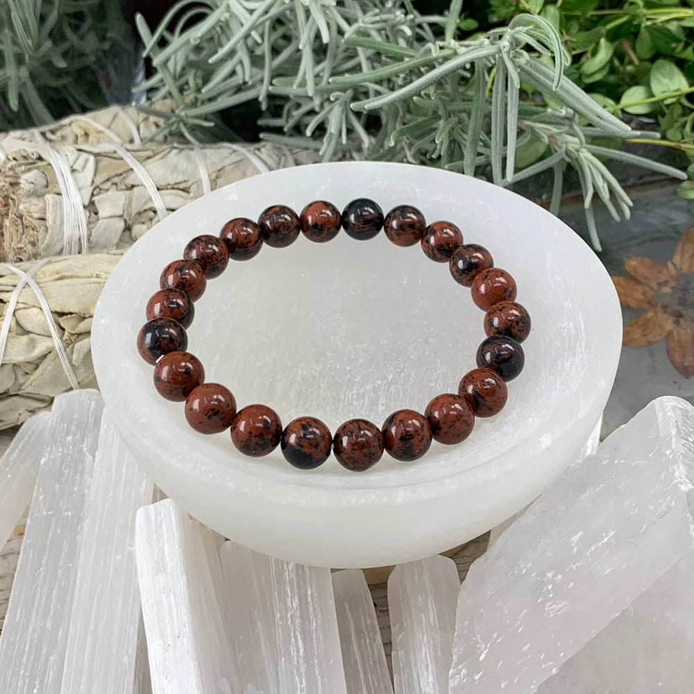 A single red obsidian mala bracelet of round mahogany-red and black beads resting in a selenite bowl