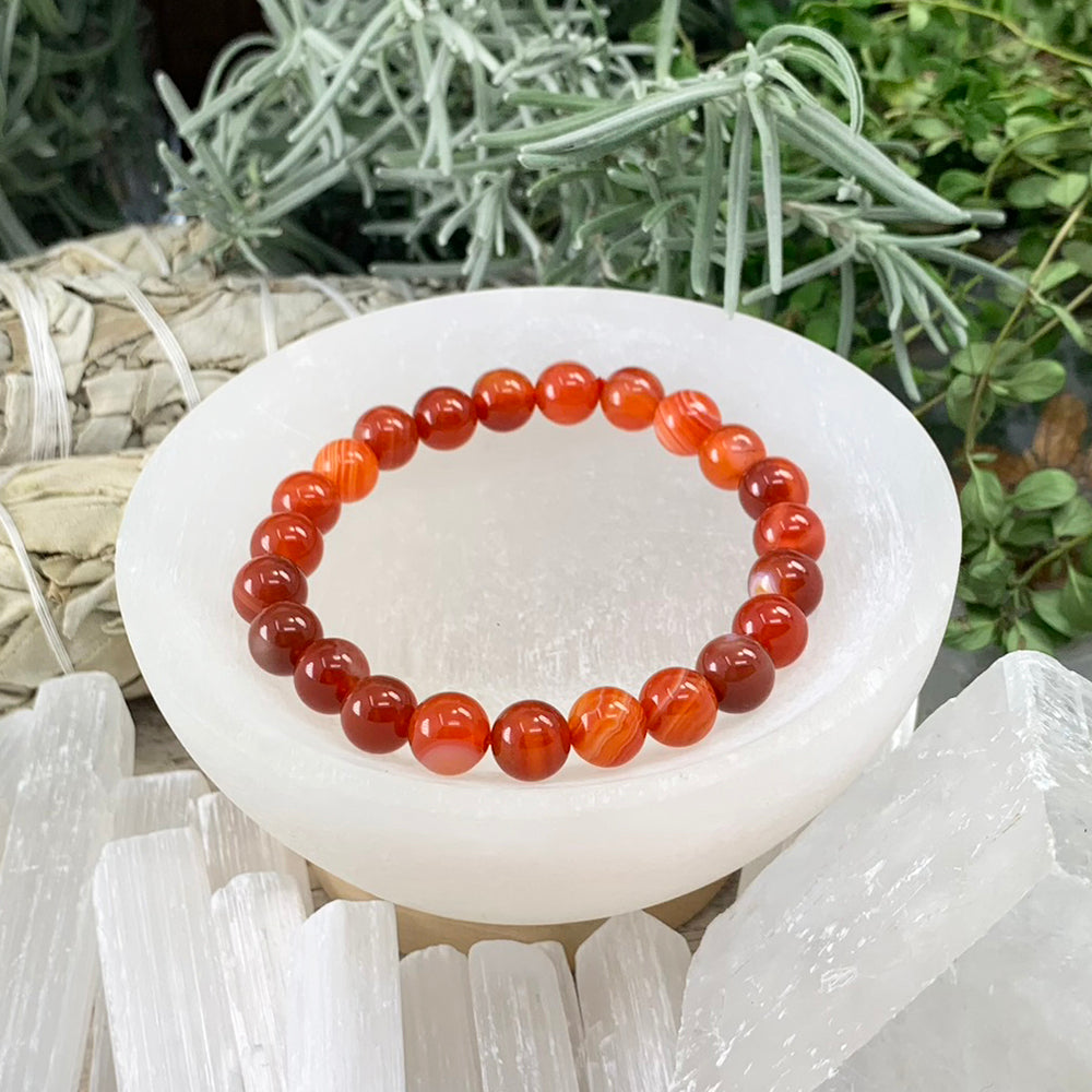 Striped red agate mala bracelet of glossy red and orange banded beads resting in a selenite bowl