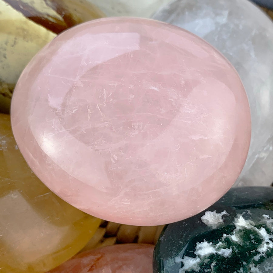 Close-up of a translucent pink rose quartz palmstone among other polished palmstones