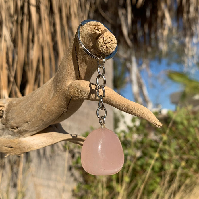 A rose quartz keychain stone on a silver-tone chain and keyring hanging from driftwood