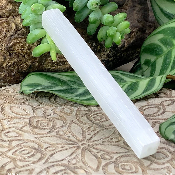 A white selenite stick lying on a carved stone surface with succulents