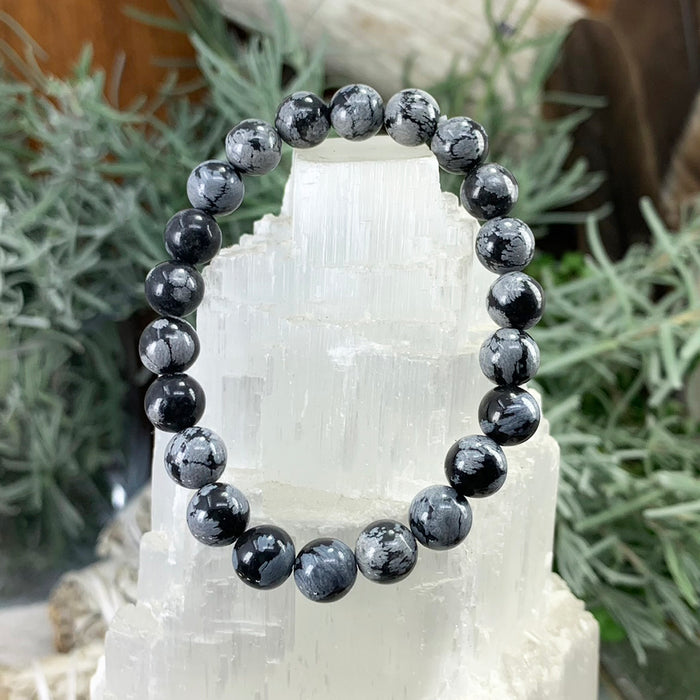 Snowflake obsidian bracelet of black beads with grey snowflake markings on a selenite tower