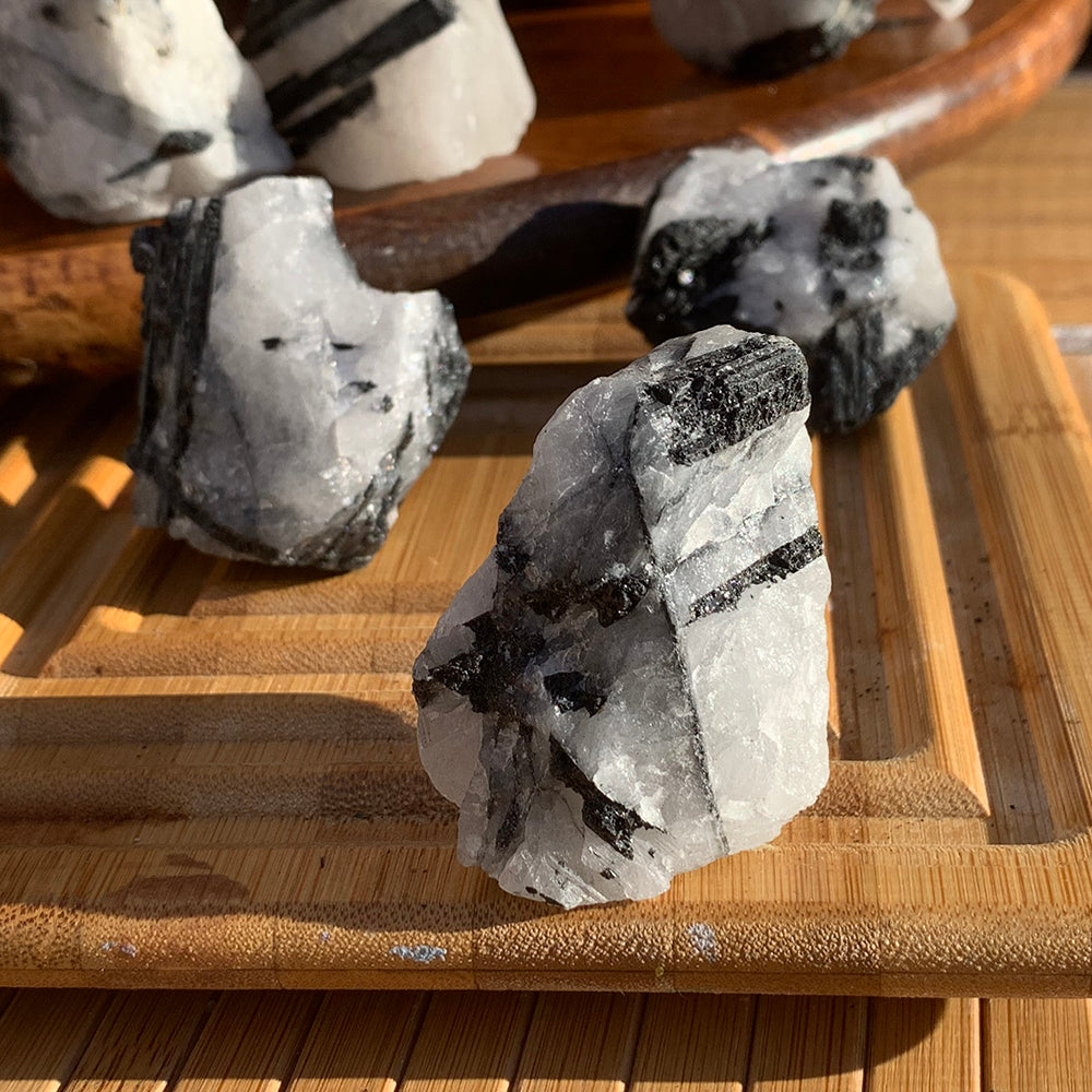 Close-up of a rough tourmalinated quartz piece, milky white quartz crossed by black tourmaline rods, on a bamboo tray